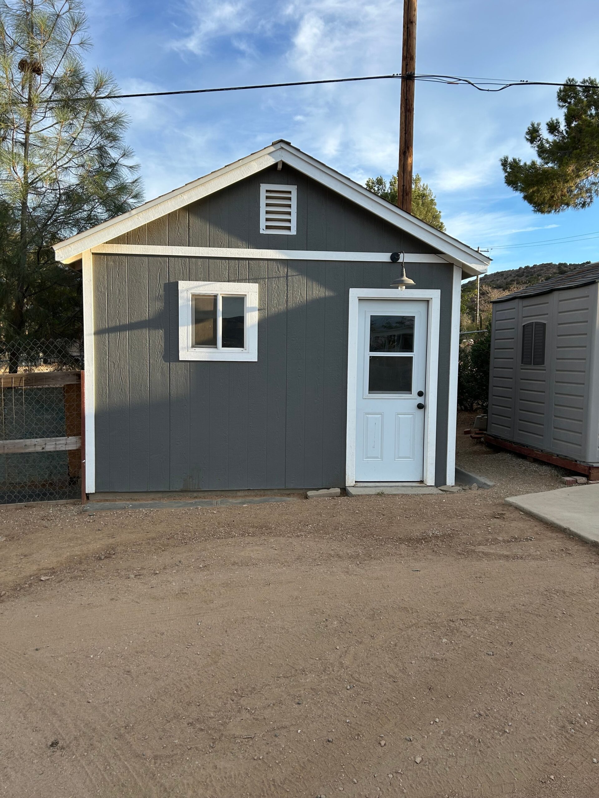 Small gray shed with a white door and window, set against a clear sky